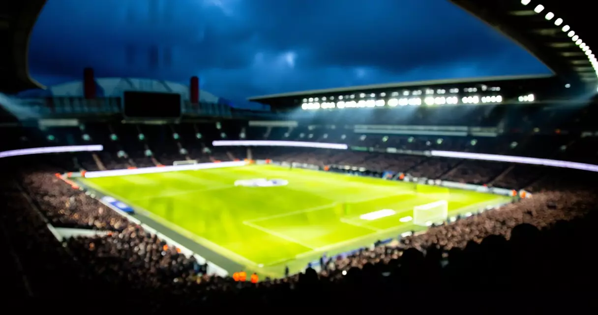 Floodlit Premier League stadium at night with packed crowd and bright pitch