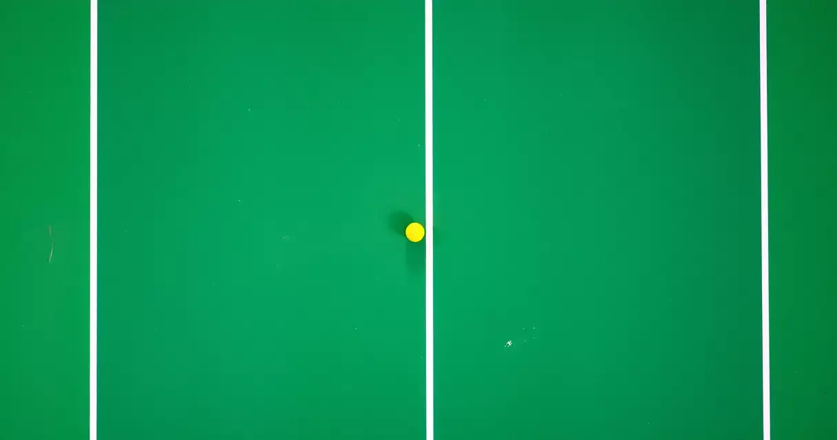 Aerial view of a hard tennis court with white lines and a yellow ball