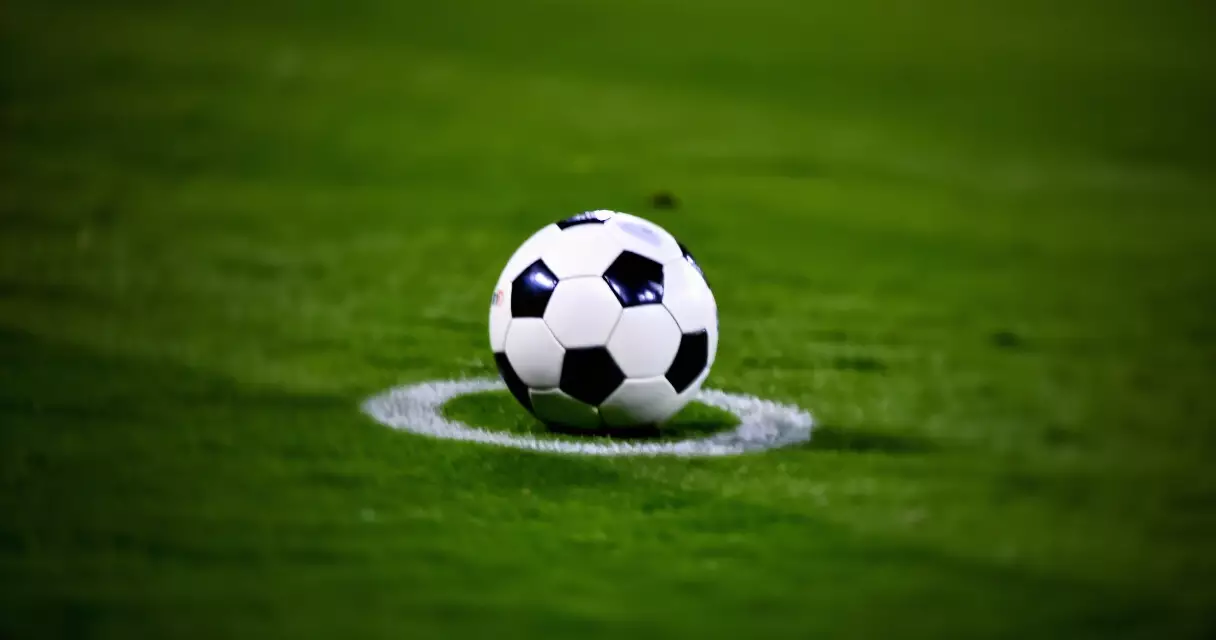 Football on the center circle of a stadium pitch under bright lights