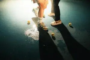 Close-up of tennis shoes and balls on wet court with dramatic lighting.