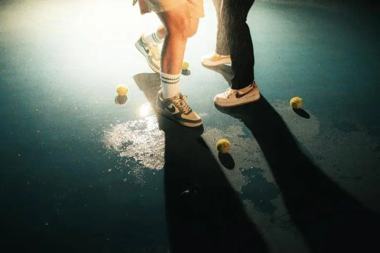 Close-up of tennis shoes and balls on wet court with dramatic lighting.